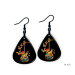 Close-up of handcrafted Stella’s Flight earrings showing vibrant butterfly-and-guitar artwork under a glossy epoxy finish.