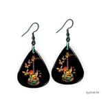 Close-up of handcrafted Stella’s Flight earrings showing vibrant butterfly-and-guitar artwork under a glossy epoxy finish.
