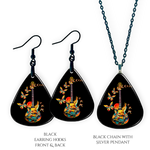Close-up of handcrafted Stella’s Flight earrings and necklace pendant set showing vibrant Golden Road Festival butterfly-and-guitar artwork under a glossy epoxy finish.