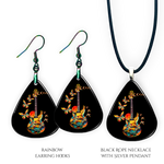 Close-up of handcrafted Stella’s Flight earrings and necklace pendant set showing vibrant Golden Road Festival butterfly-and-guitar artwork under a glossy epoxy finish.