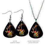 Close-up of handcrafted Stella’s Flight earrings and necklace pendant set showing vibrant Golden Road Festival butterfly-and-guitar artwork under a glossy epoxy finish.
