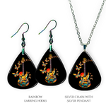 Close-up of handcrafted Stella’s Flight earrings and necklace pendant set showing vibrant Golden Road Festival butterfly-and-guitar artwork under a glossy epoxy finish.