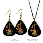 Close-up of handcrafted Stella’s Flight earrings and necklace pendant set showing vibrant Golden Road Festival butterfly-and-guitar artwork under a glossy epoxy finish.